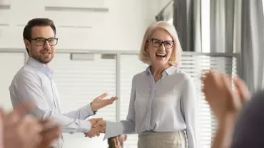 Deux personnes se serrent la main en souriant dans un bureau.