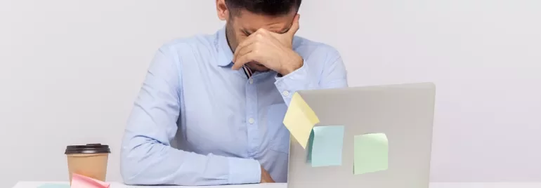 Personne avec la tête baissée devant un ordinateur portable.