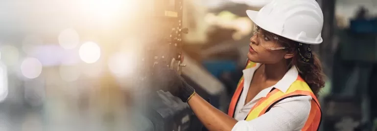 Travailleur en gilet réfléchissant et casque inspectant une machine en usine.